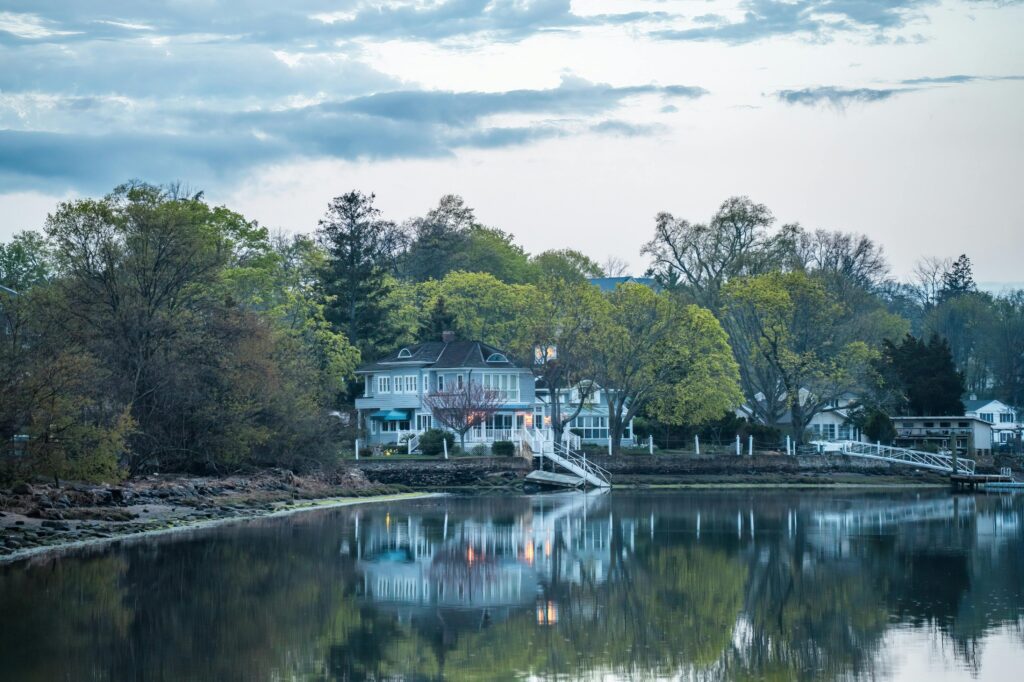 Peaceful lakeside view with a charming house and trees reflecting in the water at twilight.